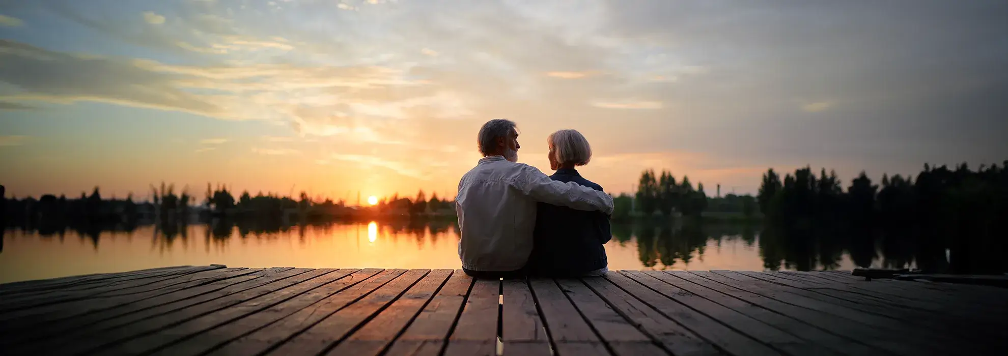 Ehepaar sitzt am See und schaut sich den Sonnenuntergang gemeinsam an.